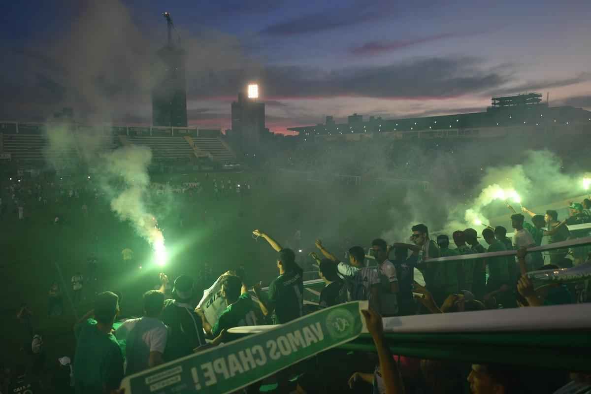 Foi na Arena ndio Cond que a Chapecoense deixou o 'anonimato' para ganhar os coraes de todos os brasileiros. Em seu estdio, o Verdo do Oeste mostrou toda sua valentia ao permanecer por trs anos seguidos na Srie A e, consequentemente, alcanar a deciso da Copa Sul-Americana. Pelo caminho ficaram gigantes como os argentinos Independiente e San Lorenzo e o colombiano Junior Barranquilla. Restava apenas o poderoso Atltico Nacional, melhor clube da atualidade na Amrica do Sul. Dentro de campo, a Chape no pde dar sequncia  sua bravura, pois acabou vitimada por um acidente areo que matou quase toda sua delegao nas proximidades de Medelln, na Colmbia. Mas, se depender do amor de uma multido, o clube renascer. A mesma Arena Cond que foi palco de trs acessos - da Srie D para a C, em 2009; da C para a B, em 2012; e da B para a A, em 2013 -  o local onde milhares de torcedores prestam as ltimas homenagens aos falecidos. Sempre, claro, com a esperana de que a agremiao se reerguer e dar continuidade ao belo trabalho recente. Vamos, vamos Chape!!! (CRDITO DAS IMAGENS: NELSON ALMEIDA/AFP)